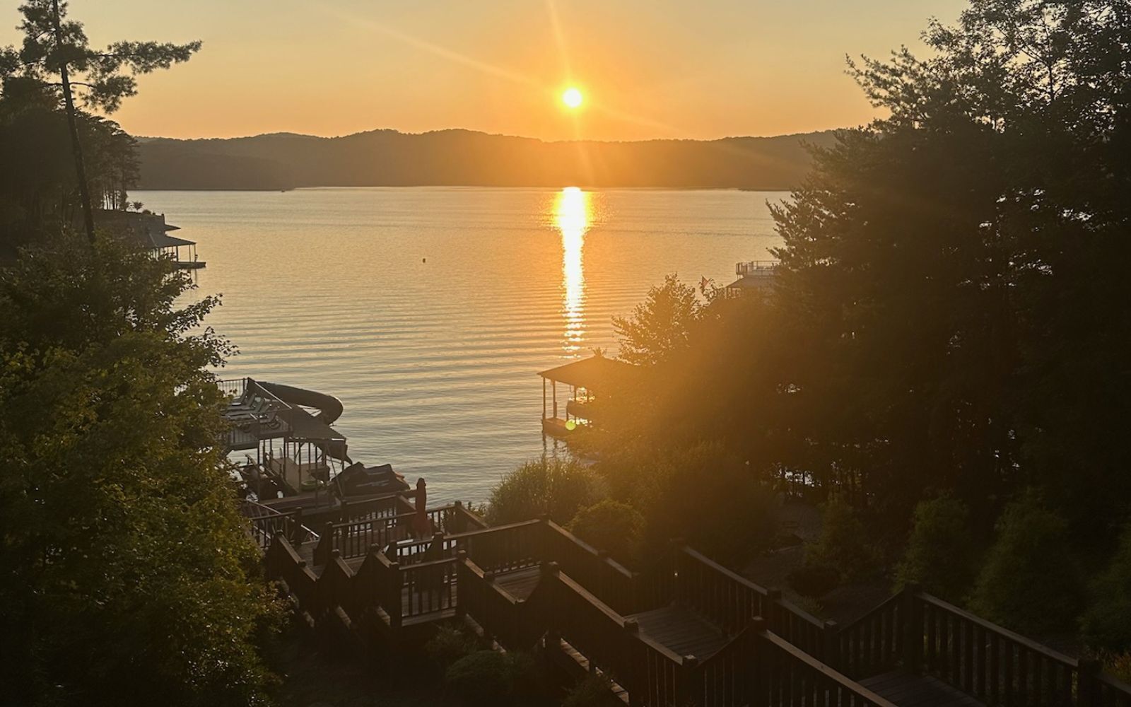 A lakeside view with a sunset, a dock, and a building with a balcony.