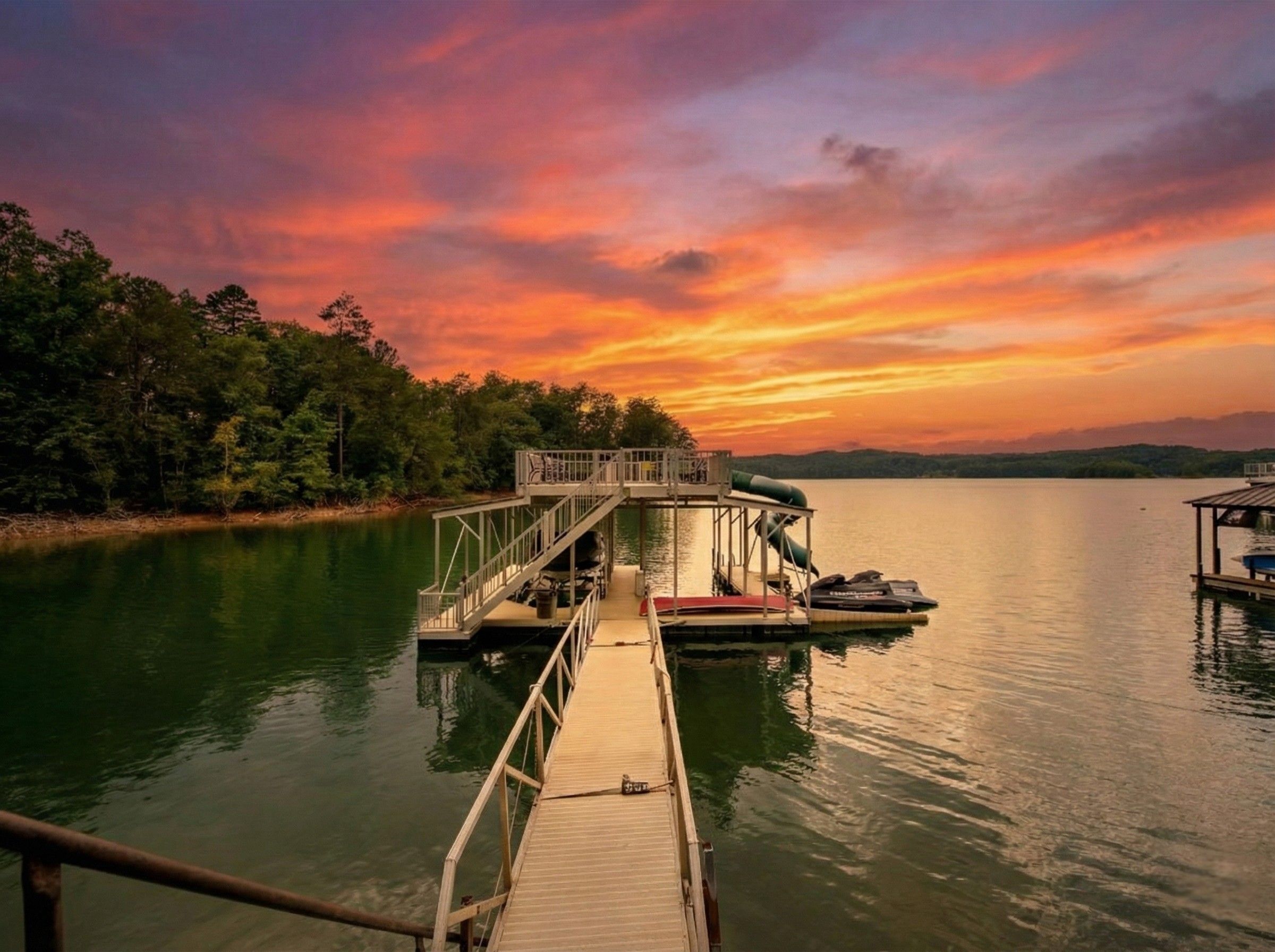 A wooden dock extending into a calm lake with a sunset in the background.