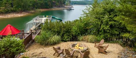 A lakeside deck with outdoor seating and a fire pit.