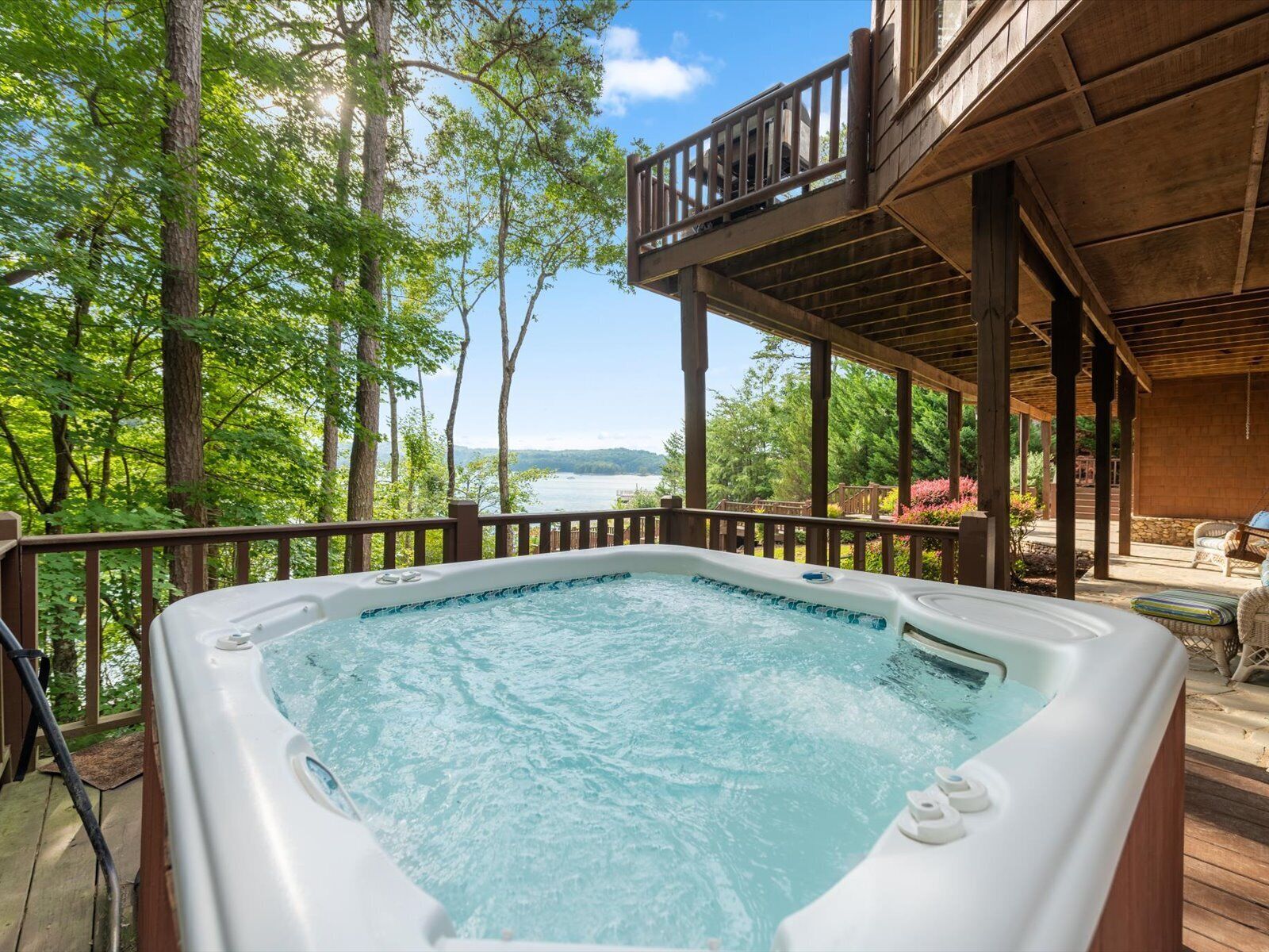A hot tub on a wooden deck with a view of a lake and trees.