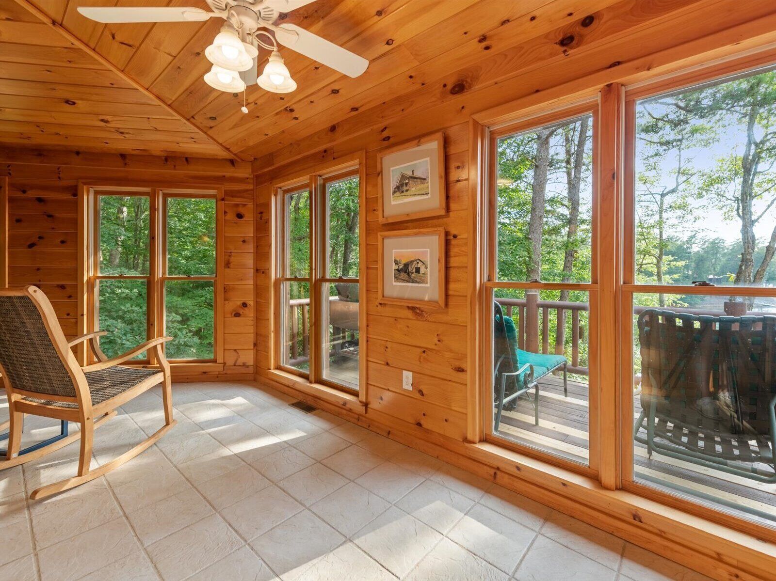 A wooden cabin interior with large windows, a ceiling fan, and a rocking chair.