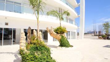 A modern building with a curved facade, large windows, and a spacious outdoor area with palm trees and greenery.