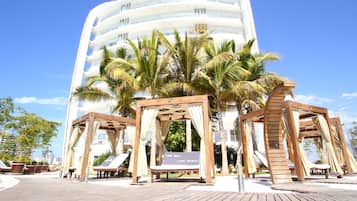 A modern hotel with multiple balconies and a wooden deck area with lounge chairs and palm trees.