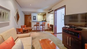 A modern living room with a sofa, a coffee table, a TV, and a dining area with chairs and a table. - Etoile Hotels - George V - Itaim Bibi (São Paulo)