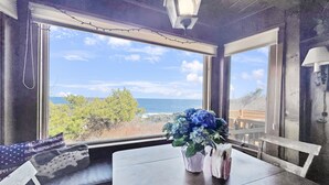 Une pièce avec vue sur l’océan, une table ornée d’un vase de fleurs et un banc agrémenté d’un coussin.
