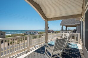 A covered porch with white railings, a blue patterned rug, and two white chairs.