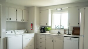 Une cuisine moderne avec des meubles blancs, un lave-vaisselle, une machine à café et une fenêtre qui laisse entrer la lumière naturelle.
