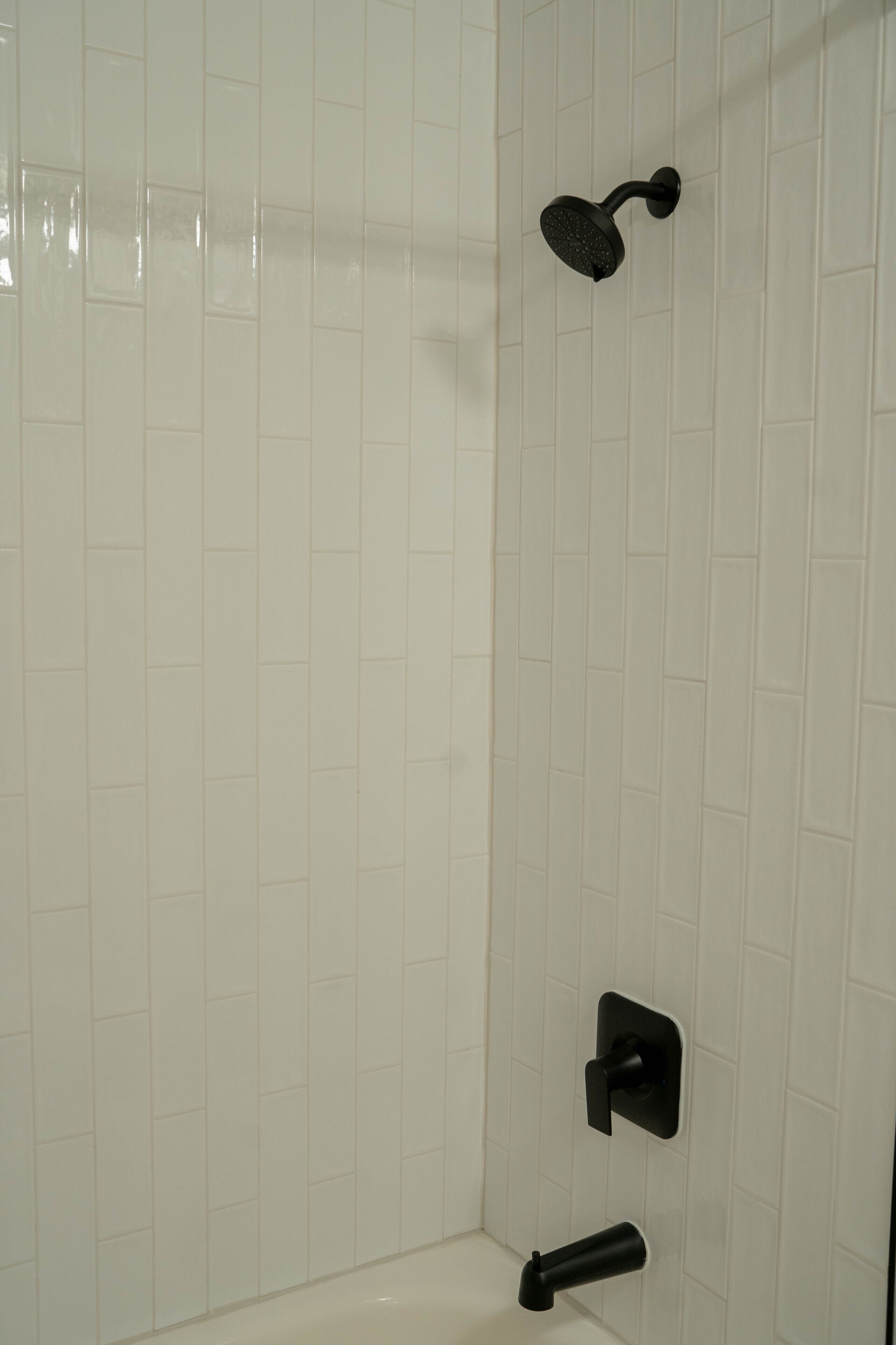 A bathroom with white tiled walls, a black showerhead, and a black faucet.