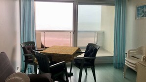 Una habitación con una mesa de comedor y sillas, un sofá, un ventanal con vista al mar y un cuadro en la pared.