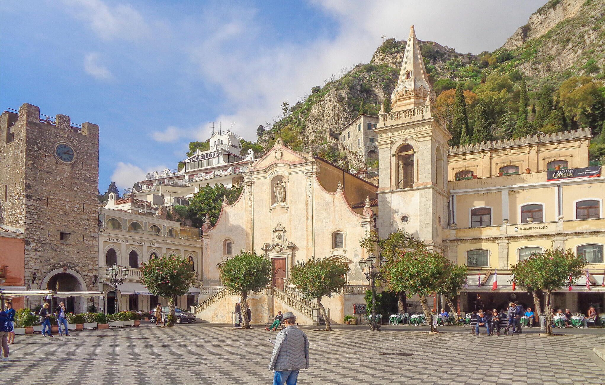 A historic square with a prominent church, a clock tower, and a hotel.
