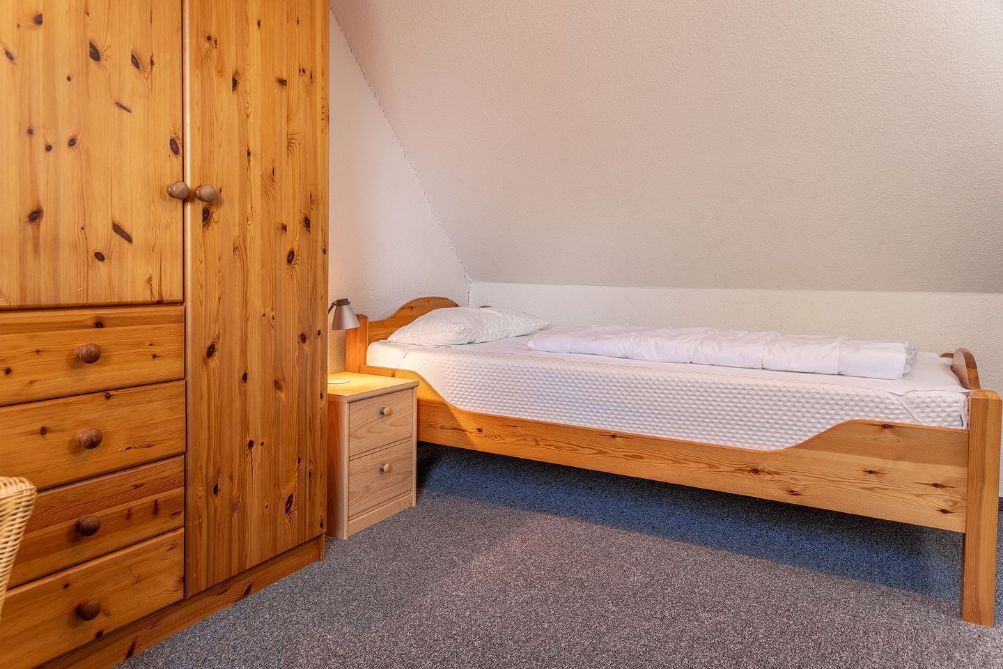 Een slaapkamer met een houten bed, een kledingkast van hout, een nachtkastje en een vloerbedekking.