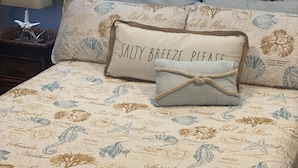 Una cama con una colcha y almohadas con motivos playeros, una lámpara y una decoración de estrella de mar en la mesita de noche.
