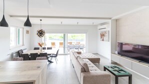 A modern living room with a large TV, a sofa, a dining area with chairs, and a kitchen area with a table and chairs. - Lovely home in Primorski Dolac (Primorski Dolac)