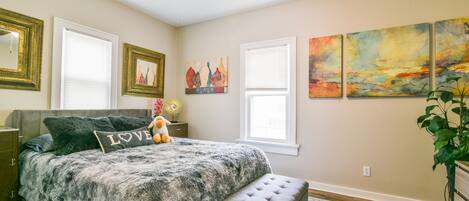 Une chambre à coucher avec un lit, un banc, un ventilateur de plafond et des œuvres d’art accrochées aux murs.