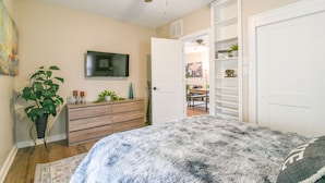 Een slaapkamer met een bed, een plafondventilator, een televisie, een dressoir en een deur naar een eetruimte.