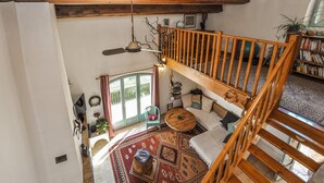 Un loft espacioso con techo alto, una escalera de madera, un rincón de estar acogedor con alfombra estampada y una estantería llena de libros.