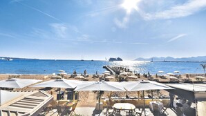 Un restaurante junto a la playa con terraza, sombrillas y vistas al mar y las montañas.