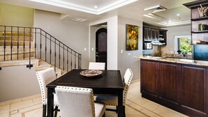 A modern kitchen with dark wooden cabinets, a granite countertop, and a dining area with a black table and white upholstered chairs. - Oceanview Penthouse in Heart of Tamarindo - Perfect Location & Comfort (Tamarindo)
