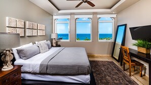 A bedroom with a bed, a ceiling fan, a desk with a TV, and large windows with a view of the ocean. - Oceanview Penthouse in Heart of Tamarindo - Perfect Location & Comfort (Tamarindo)