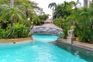 A pool area with a thatched-roof bridge, surrounded by lush greenery. - Oceanview Penthouse in Heart of Tamarindo - Perfect Location & Comfort (Tamarindo)