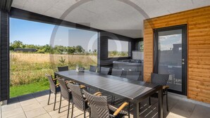 A modern outdoor dining area with a long table and chairs, a built-in grill, and a view of a natural landscape. - 4 bedroom beautiful home in Løgstrup (Løgstrup)