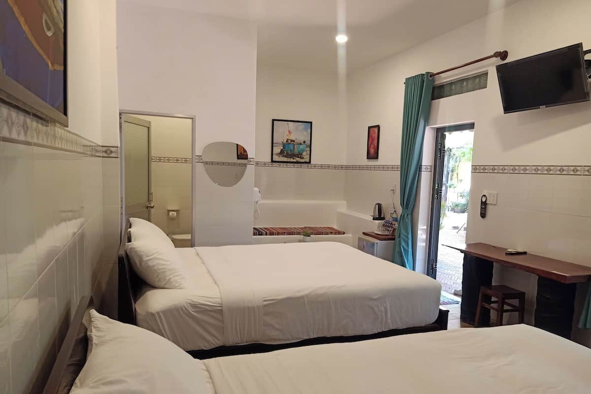 Quarto de hotel com duas camas, banheiro, uma secretária pequena e televisão fixada na parede.