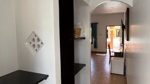 Un pasillo con suelo de madera, un estante negro y una pared blanca con toma de corriente.