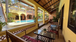 Zona junto a la piscina con una mesa de vidrio, asientos acolchados y vista a una piscina y un edificio.