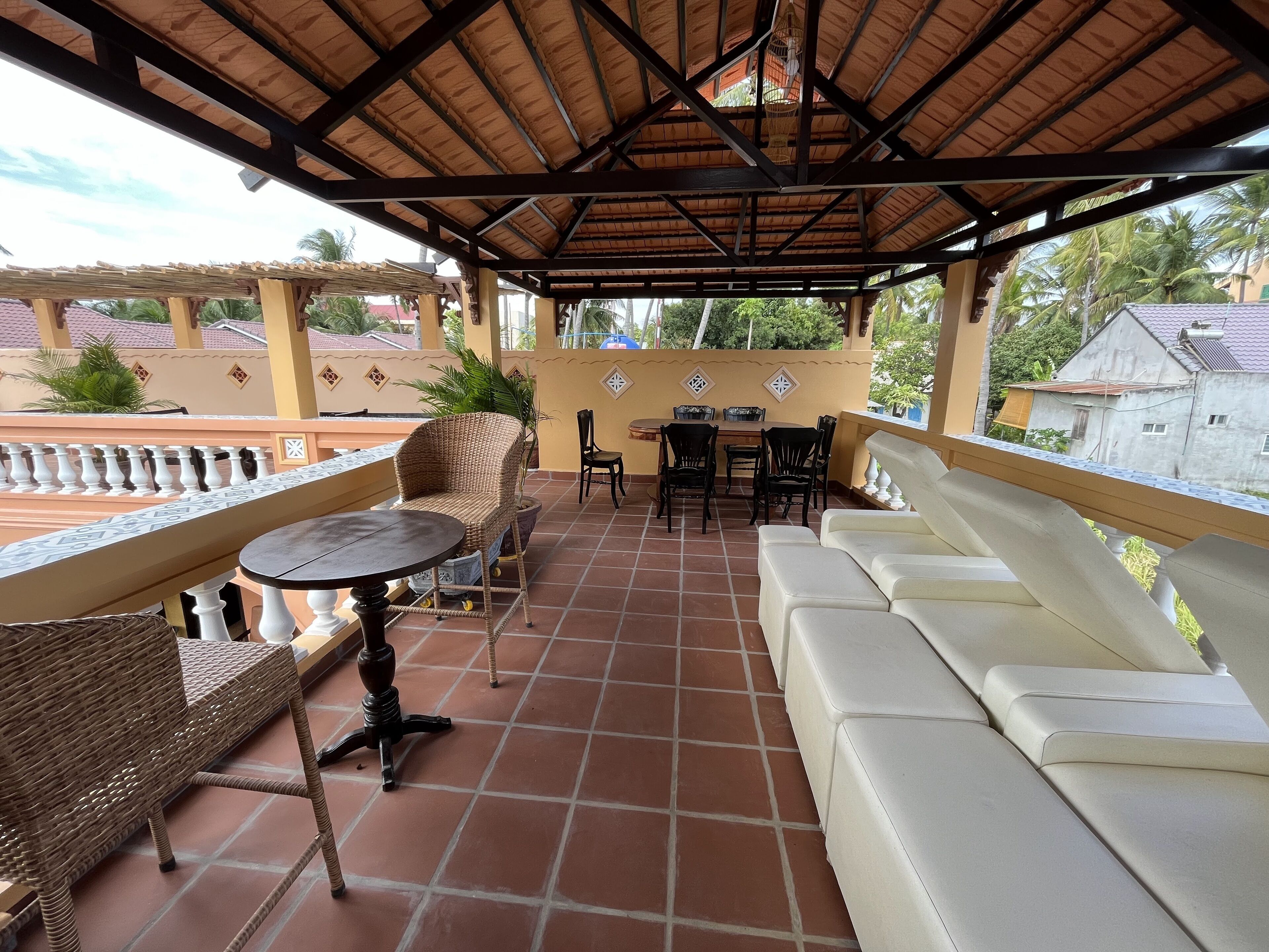 A covered patio area with a tiled floor, a white sofa, wicker chairs, and a small round table.