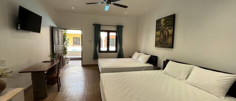 A hotel room with two beds, a desk, a ceiling fan, a TV, and a painting on the wall.