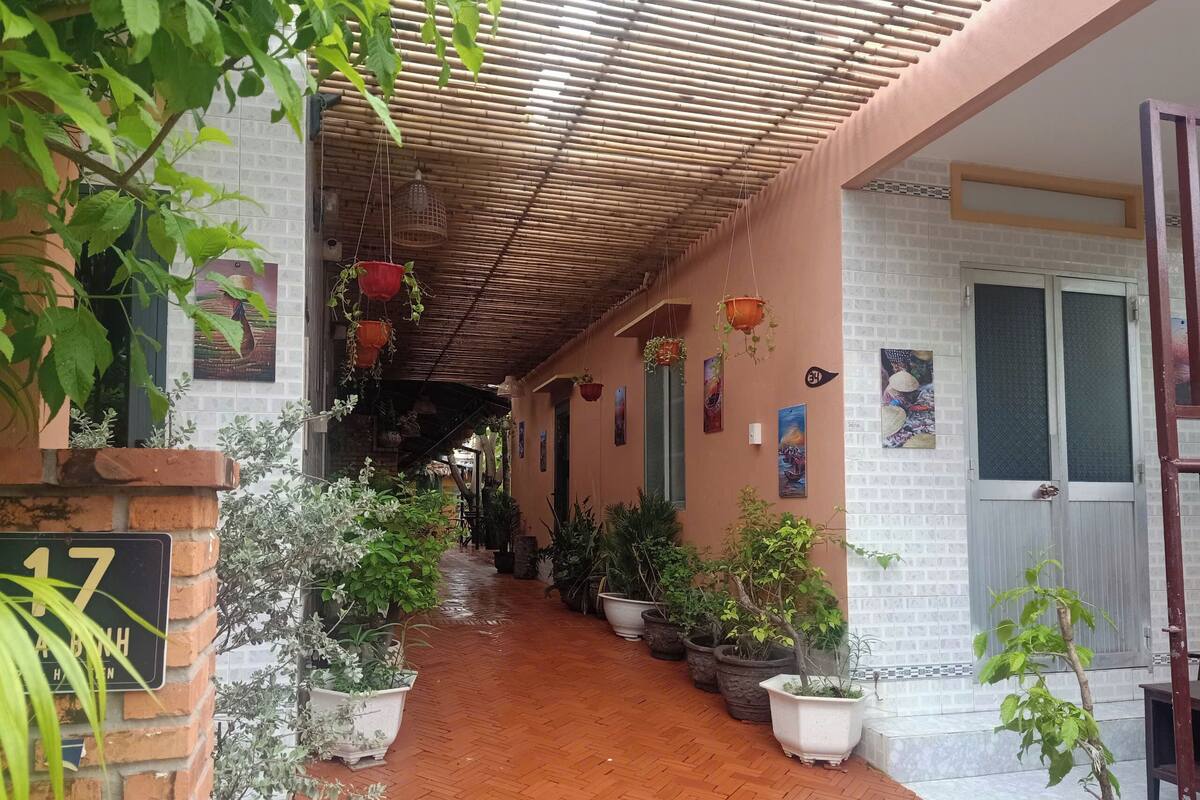 Uma galeria coberta com plantas em vasos, uma parede de tijolos com uma placa e uma porta com janela.