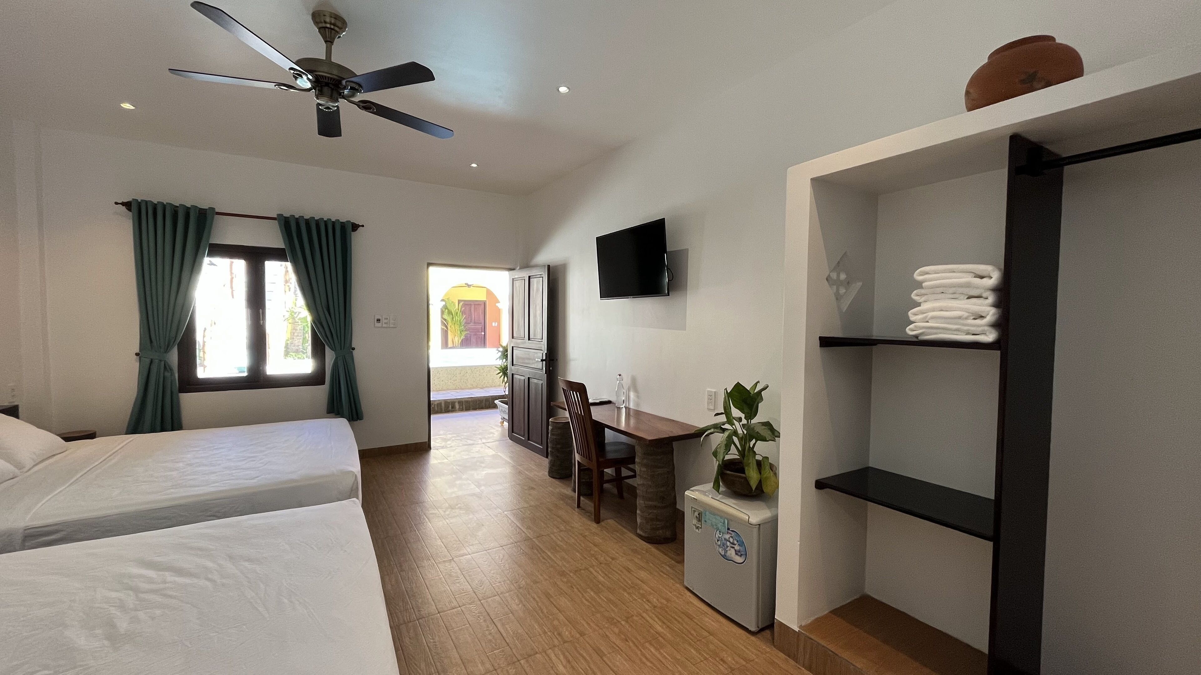 A hotel room with a bed, a desk, a chair, a TV, and a shelf with towels.
