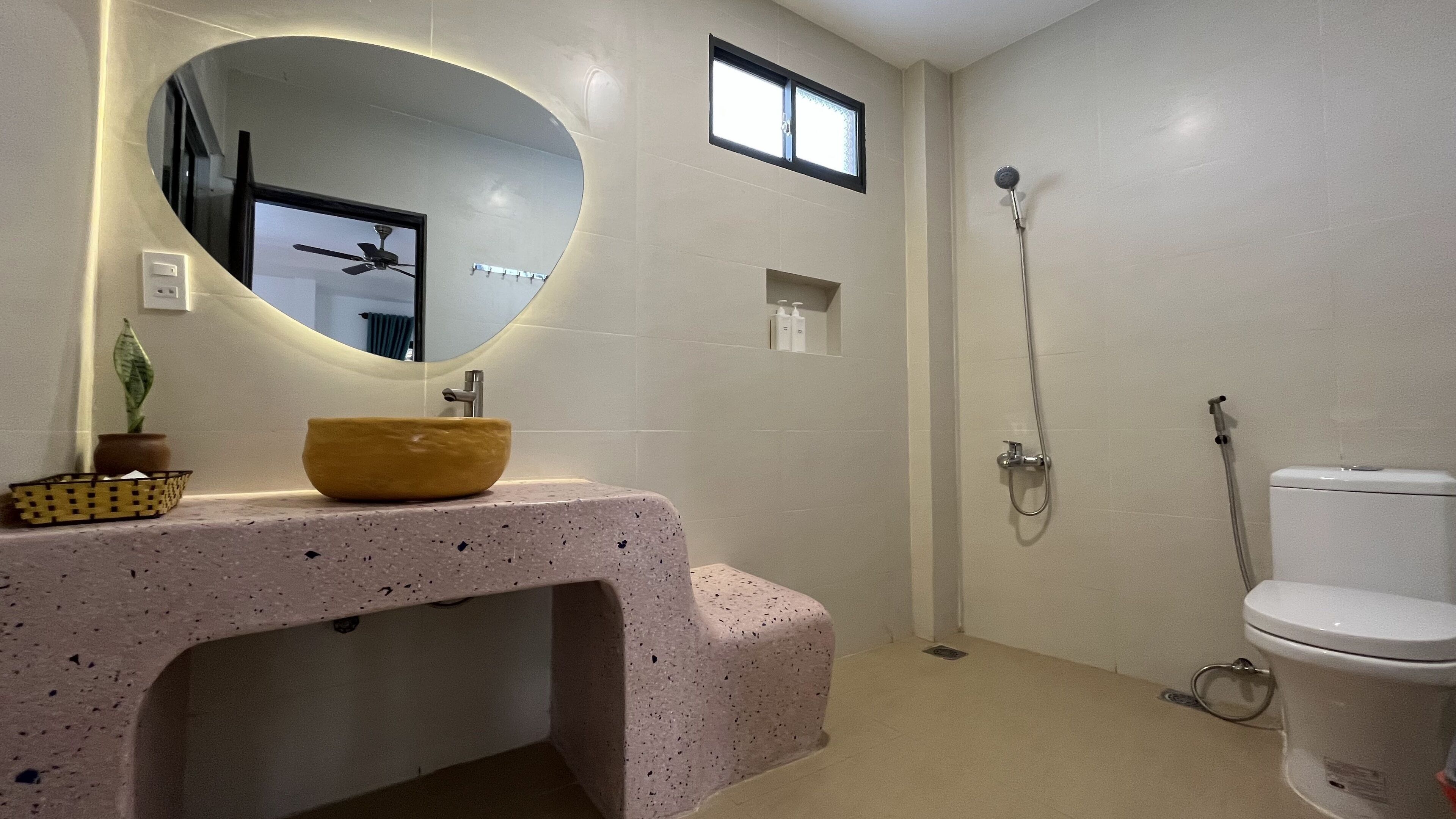 Un baño con un espejo redondo, un lavabo sobre encimera, ducha e inodoro.