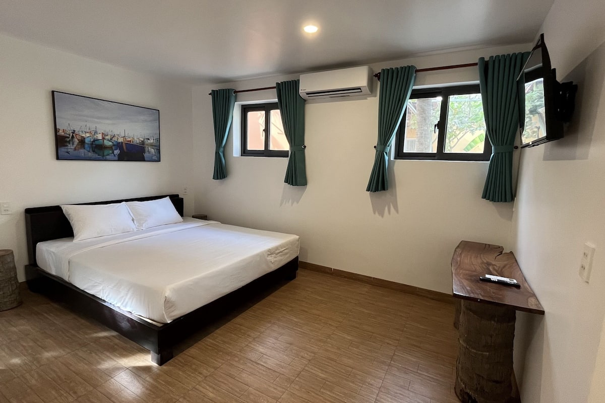 Quarto com cama, televisão na parede e janela com cortinas.
