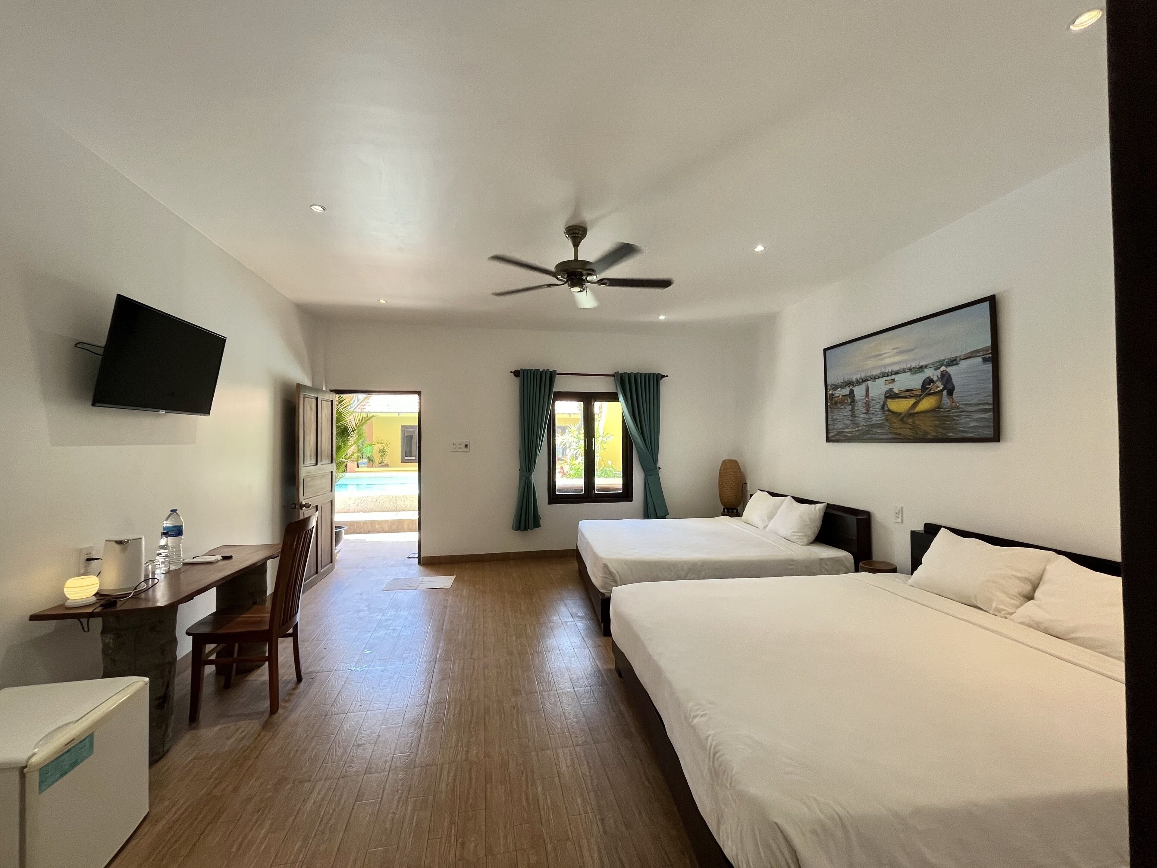 A hotel room with two beds, a desk with a chair, a television, and a ceiling fan.