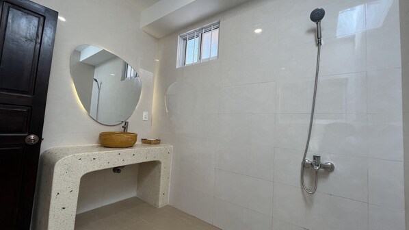 Un baño con un espejo redondo, un lavabo color beige y una ducha.