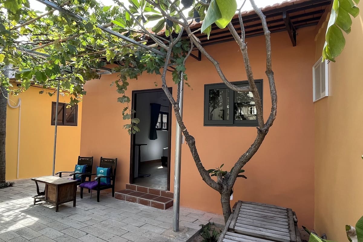 Um pátio com uma mesa e cadeiras de madeira, um banco de madeira pequeno e uma árvore.