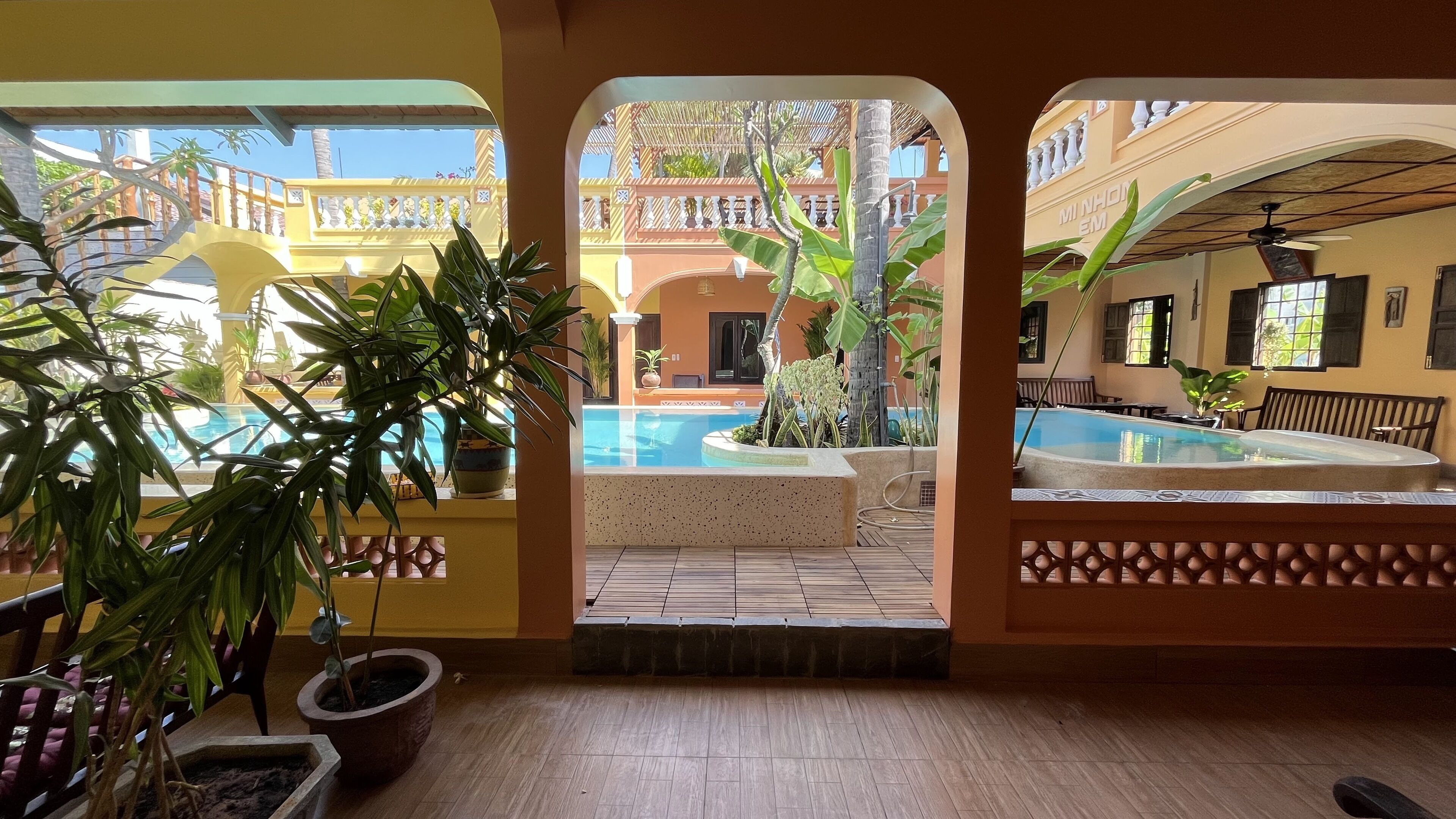 Zona de piscina con dos piscinas, rodeada de plantas en macetas y una terraza de madera.