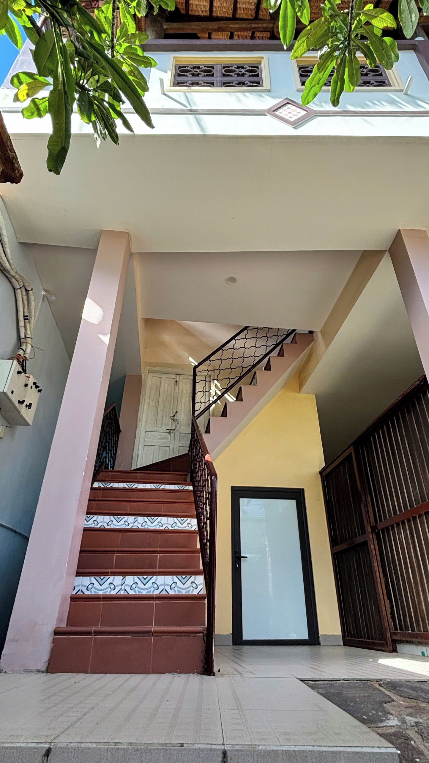 Eine Treppe führt zu einer zweiten Etage mit einem gemusterten Fliesenboden, einer Tür und einem Metallgeländer.