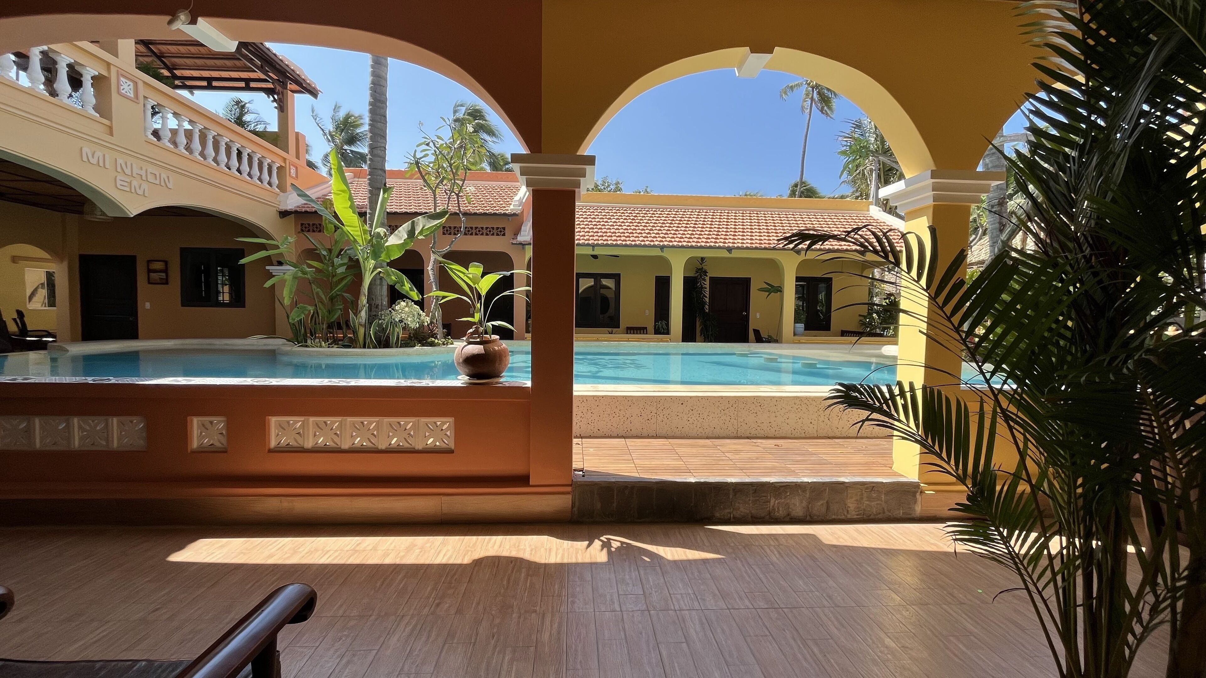 Un área de piscina con suelo de baldosas, una piscina y una zona de estar cubierta con barandilla.