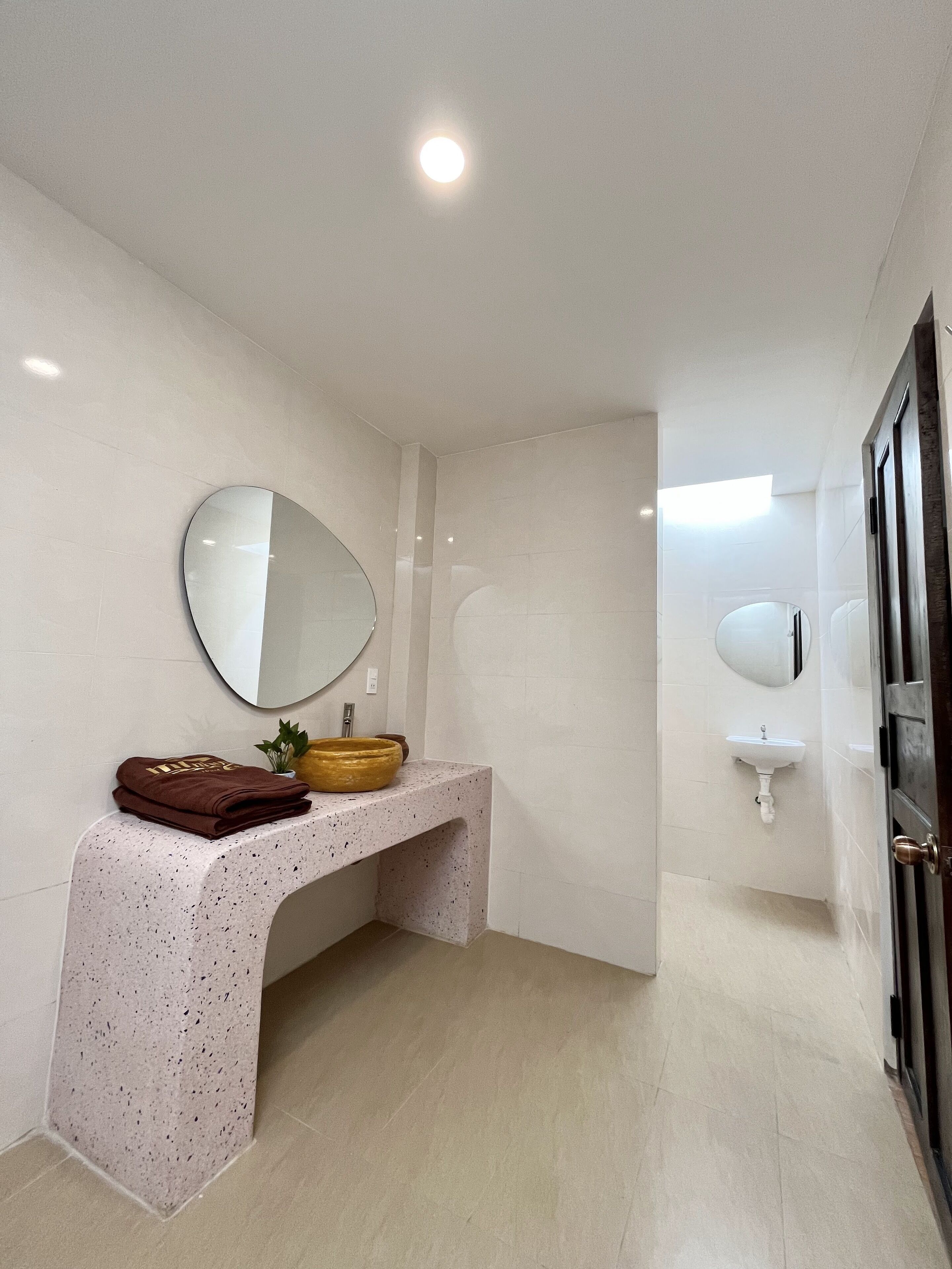 Un baño moderno con tocador de mármol, espejo redondo, lavabo y puerta.