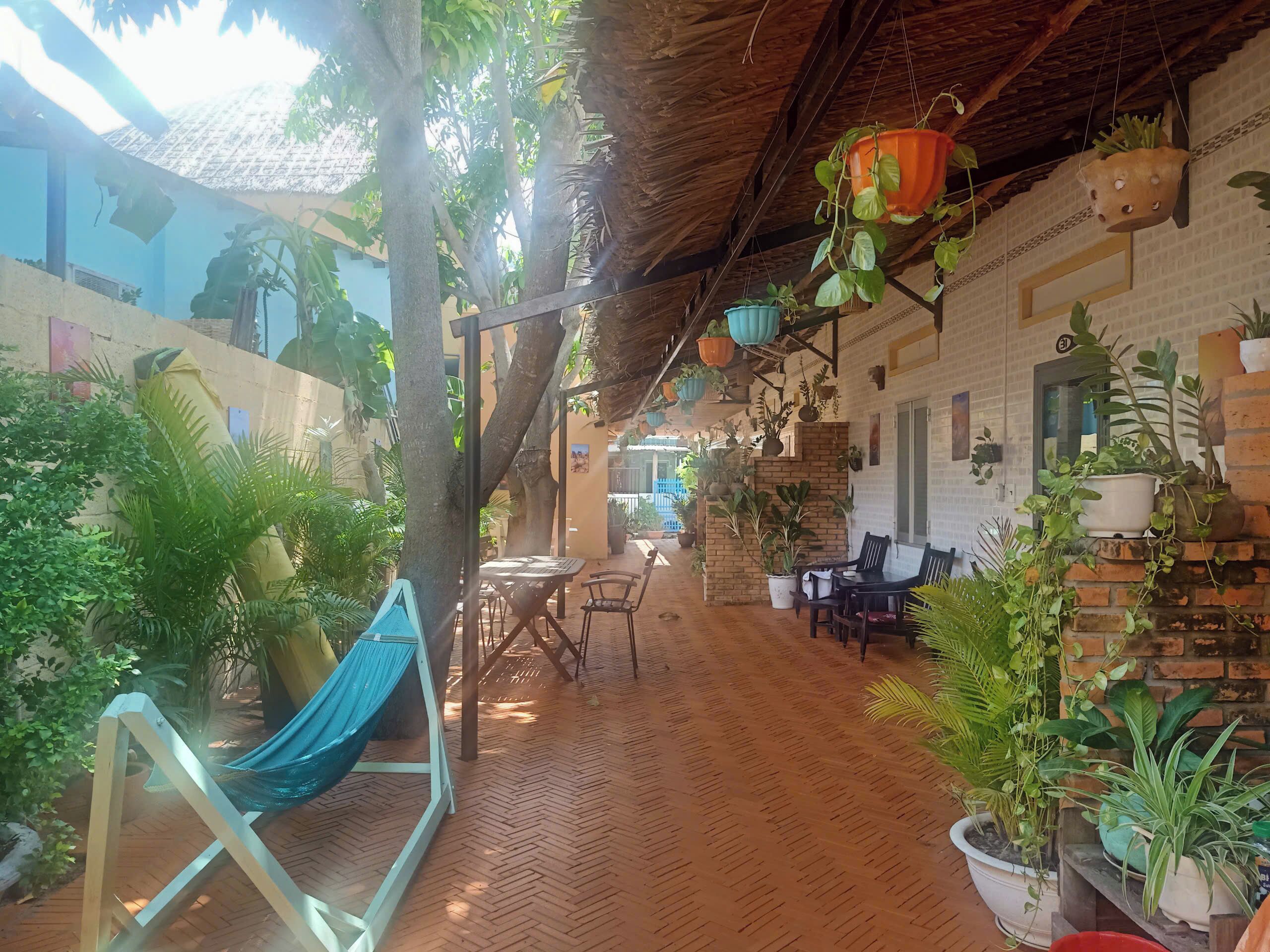 A covered outdoor area with a hammock, tables, chairs, and various potted plants.