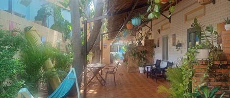 A covered outdoor area with a hammock, tables, chairs, and various potted plants.