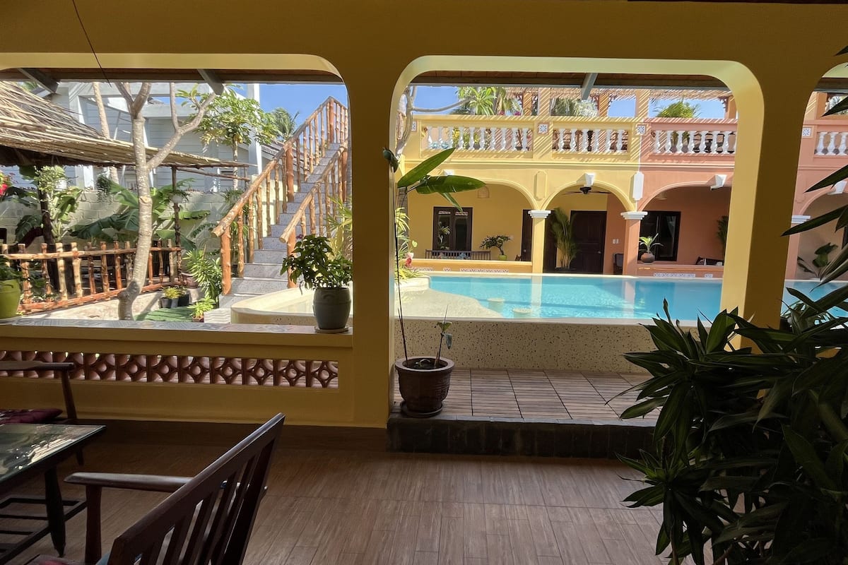 Área à beira da piscina com vista para a piscina, plantas em vasos e uma escadaria para um terraço.