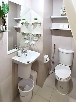A bathroom with a white sink, mirror, and toilet. There are shelves with toiletries and a plant.