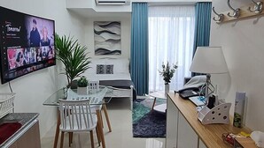 A modern living room with a flat-screen TV, a dining area with a glass table and chairs, a sofa, and a kitchen area with a microwave and a lamp. - Inspiria Condo Units beside Abreeza Mall Davao (Davao)