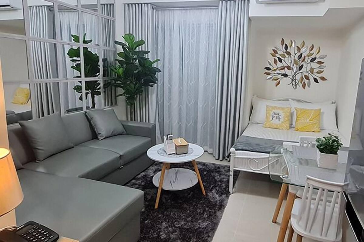 Un salon moderne avec un canapé gris, une petite table ronde, un fauteuil blanc et un élément décoratif mural.