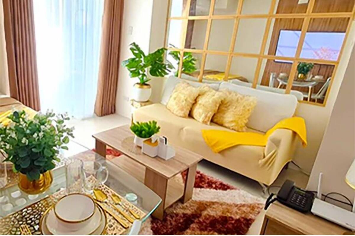 Un salon moderne avec un canapé, une table basse et des plantes. On y trouve également un coin repas avec une table dressée pour deux personnes.