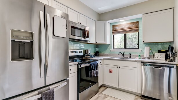 A modern kitchen with stainless steel appliances, white cabinetry, and a window with blinds.
