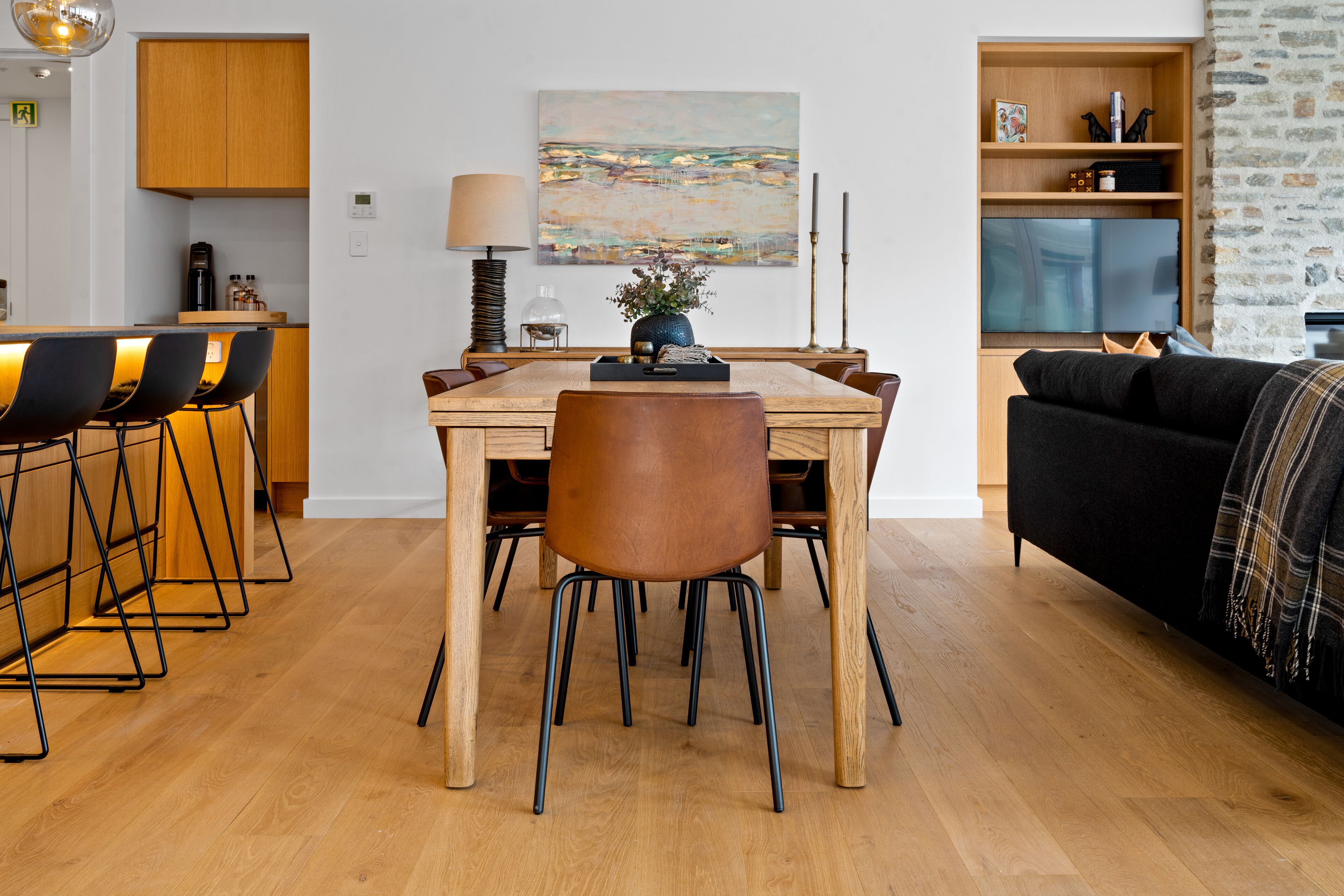 Een moderne keuken met een eethoek, houten keukenkastjes en een zwarte bank.
